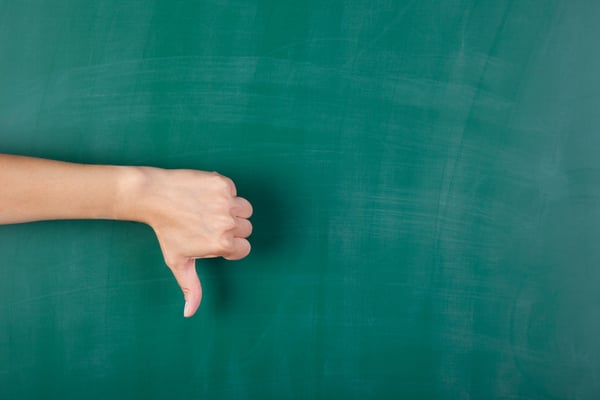 Closeup of womans hand gesturing thumbs down against chalkboard